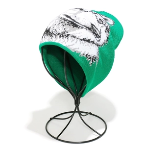 Detail of green knit beanie featuring a wolf jacquard pattern on a metal display stand
