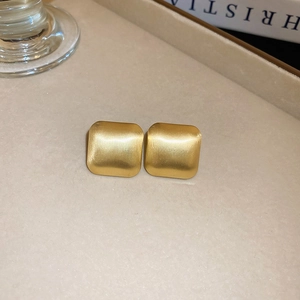 Detailed view of square matte gold stud earrings on a textured tray with warm lighting