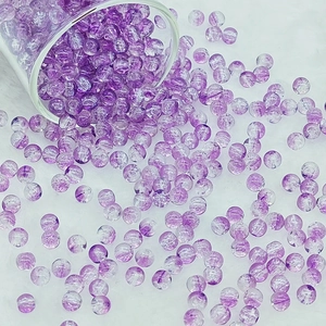 Detailed view of purple crackle glass beads scattering on a white velvet surface