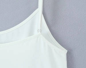Détail d'une fine bretelle blanche avec anneau métallique sur une robe caraco minimaliste