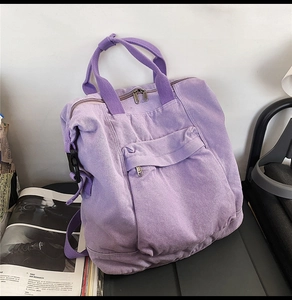 Purple canvas backpack with top handles and front zipper pocket in a casual lifestyle setting