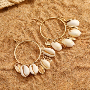 Detailed shot of golden hoop earrings with natural white shells on beach sand