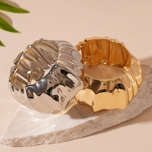 Polished gold and silver wide crinkled metal cuff bracelets on white stone base
