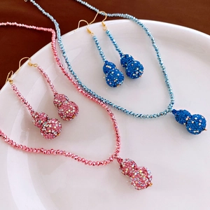 Macro shot of diamond-encrusted gourd pendant necklace and earrings in blue and pink