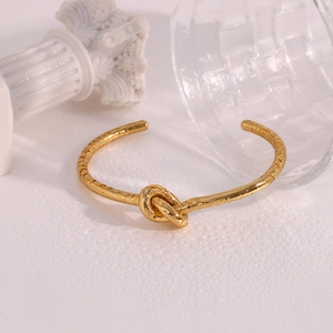 Detailed view of gold knotted open bangle featuring a unique hammered texture finish