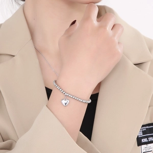 Nahaufnahme eines silbernen Perlenarmbands mit Herzanhänger am Handgelenk eines Models
