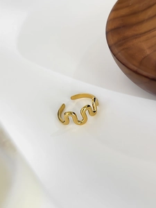 Detail of adjustable gold wavy ring displayed on a minimalist white and wood background