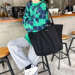 Close-up of the black canvas tote bag worn by a model in a modern urban cafe setting