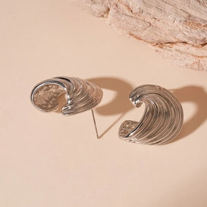 Macro shot of silver C-shaped wave textured earrings on a minimalist stone display