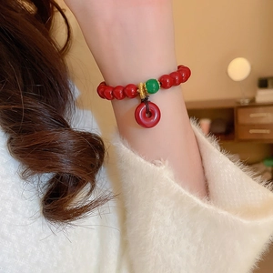 Gros plan d'un bracelet en perles rouges avec perle verte et pendentif nœud sur un poignet