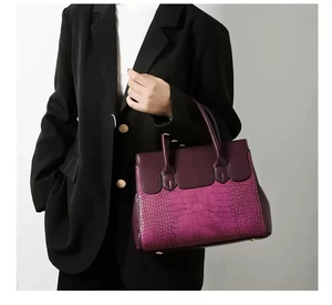 Detailed view of burgundy crocodile-embossed leather tote bag held by a professional model