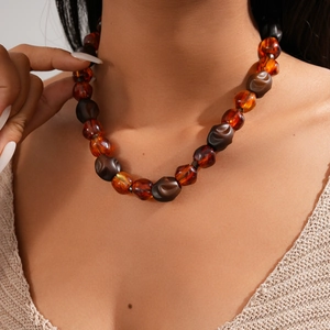 Macro detail of amber and dark brown resin beads on an acrylic statement collar necklace