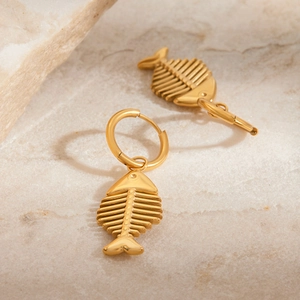Detailed close-up of golden fishbone earrings on a minimalist stone surface