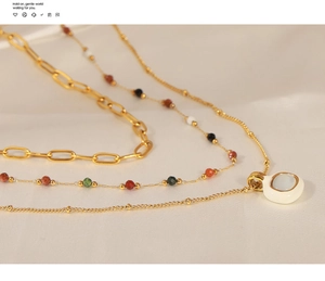 Macro shot of layered gold chain necklace with natural stones and white enamel pendant