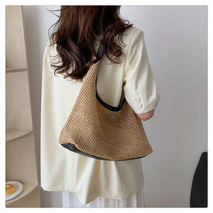 Detail of woven straw tote bag with black leather trim worn on the model's shoulder