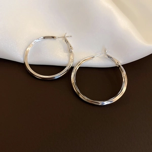 Macro shot of polished silver geometric hoop earrings resting on white silk fabric