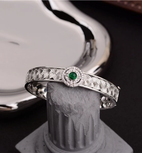 Detailed macro of a silver lace woven bracelet with green gemstone and white zircons