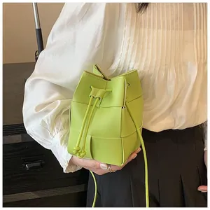 Detail of lime green woven drawstring bucket bag showing leather texture and strap