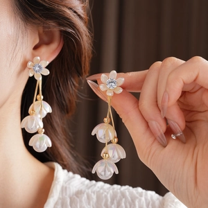 Detail of long tassel earrings featuring floral studs and gold chain with pearlescent beads