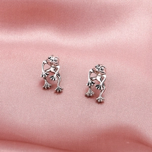 Macro shot of silver frog earrings displayed on elegant pink silk textured fabric