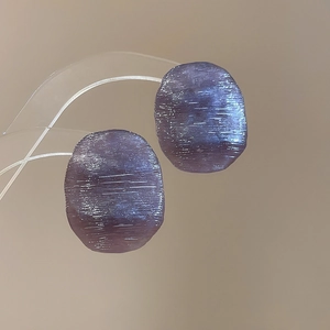 Macro detail of dark purple resin earrings with elegant horizontal brushed textures