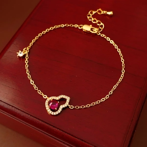 Detailaufnahme des 18K vergoldeten Armbands mit rotem Zirkon auf dunklem Holz