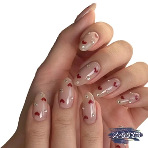 Handmade nude pink almond press-on nails with red heart patterns and shiny rhinestones
