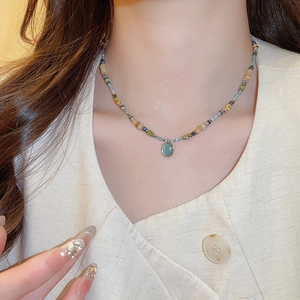 Close-up of a beaded stone necklace with an oval blue cat-eye pendant on a female neck