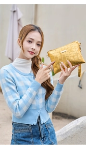 Detail of gold faux crocodile texture on luxury envelope clutch bag held by model