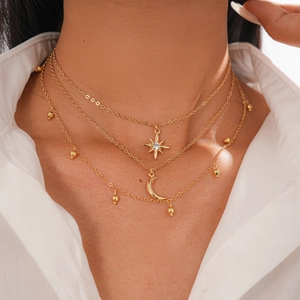 Detail of three-layer gold necklace featuring crystal star and crescent moon pendants