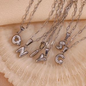 Flat lay of multiple silver initial bubble pendants Q N I Y S G on paperclip chains