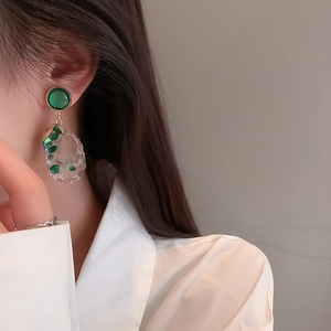 Macro detail of irregular resin drop earring with green stones and gold-toned metal rim