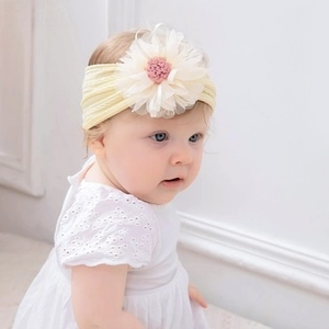 Detail of baby headband with a large white tulle flower and pink pompom on yellow rib knit