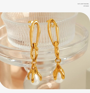 Detail of 18K gold chain earrings with drop pearls hanging from a glass vessel edge