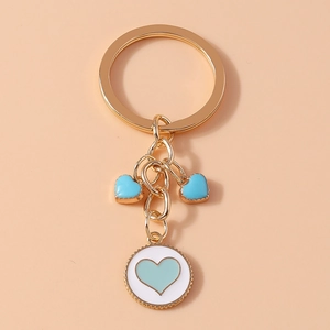Detail of gold keychain with blue heart charms and round white pendant on peach background