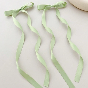 Close-up of two light green satin ribbon bow hair clips with long elegant streamers
