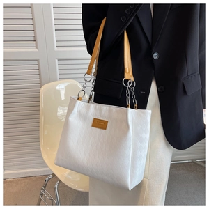 Close-up of white quilted tote bag featuring metal chain and leather shoulder strap detail