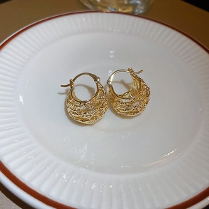 Detailed close-up of gold woven texture heart earrings on a decorative ceramic dish