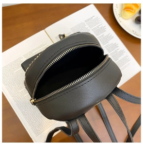 Top view detail of black leather mini backpack with gold rivets and metallic zipper on a desk