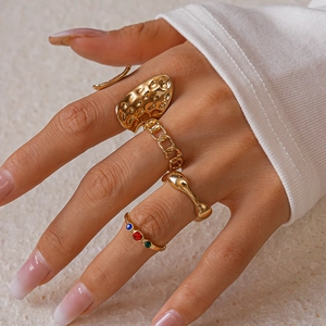 Detail of three-piece gold ring set with chain element, hammer texture, and colored gems