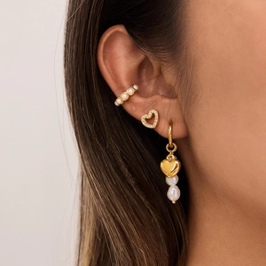 Detailed view of gold heart stud and pearl ear cuff set on a model ear