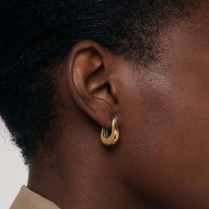 Close-up of wavy gold stainless steel hoop earring shown on ear with high-polish finish