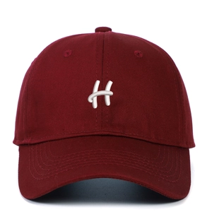 Close-up of white letter H embroidery on dark red cotton baseball cap with ventilation holes