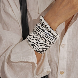 Detail of zebra pattern faux leather wide cuff bracelet worn with a white linen shirt