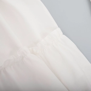 Close-up of white chiffon V-neck dress showing delicate ruffle hem and pleated details