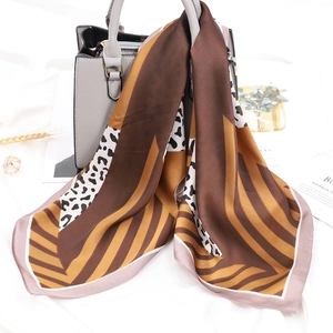 Dettaglio di un foulard in raso con stampa leopardata e righe su una borsa a mano grigia