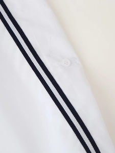 Detail showing white fabric with black stripes and a button on this sporty blouse