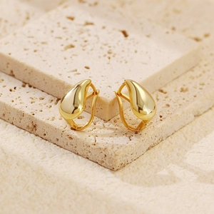Macro shot of minimalist gold teardrop earrings on textured stone base with high gloss