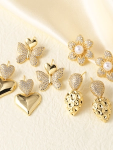 Detalle de pendientes chapados en oro con mariposas, corazones y perlas sobre seda