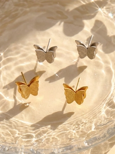 Macro detail of gold and silver butterfly earrings showing matte finish and water ripples